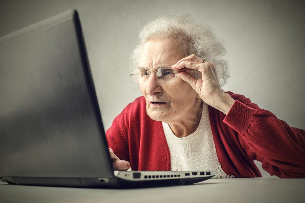 Äldre dam som rättar till sina glasögon framför lapptoppen.